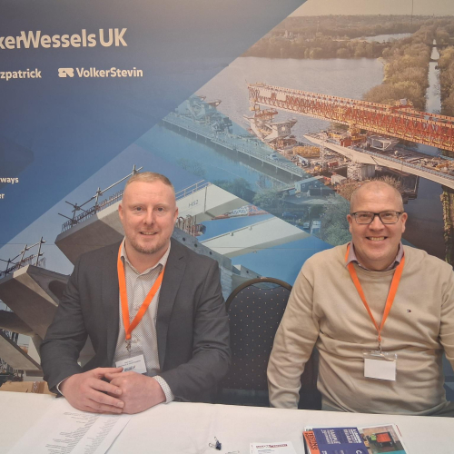 Two men sat at table with a blue banner behind them with construction photos on - VolkerTrenchless Solutions