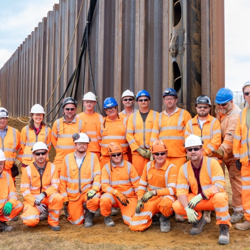Group photo of men and women in orange hi vis construction workwear and hard hats
