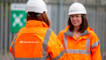 Two female employees in orange PPE and white hardhats