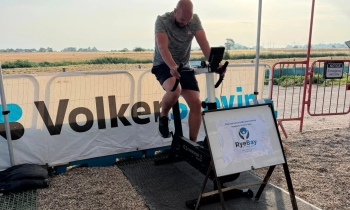 Man in grey t-shirt and black shorts on an exercise bike under a canopy