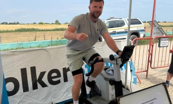 Man wearing a grey t-shirt and black shorts on an exercise bike under a canopy