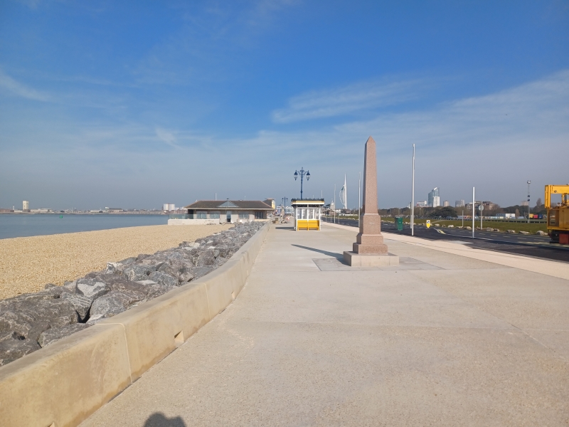 Promenade with beach to the left and monument and ornate yellow shelter in the background