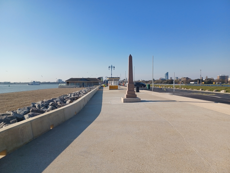 Promenade with beach to the left and monument in the background. Blue skies