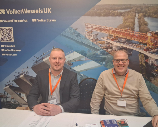 Two men sat at table with a blue banner behind them with construction photos on - VolkerTrenchless Solutions