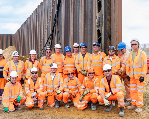 Group photo of men and women in orange hi vis construction workwear and hard hats