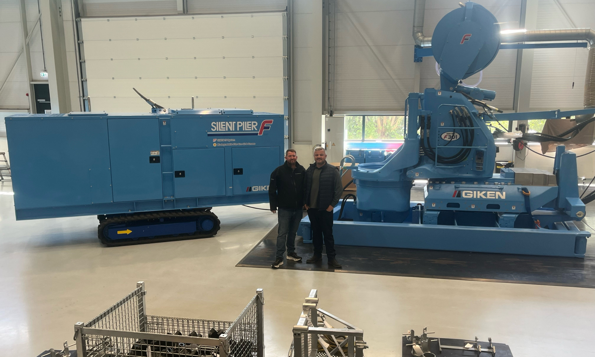 Large two piece piling machine in blue with two men stood in front of it